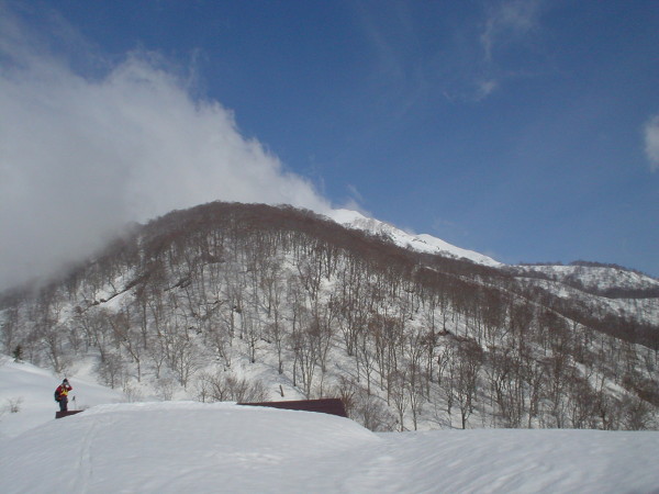 雪に埋もれる雨飾高原、雲の間から雨飾山がのぞく。